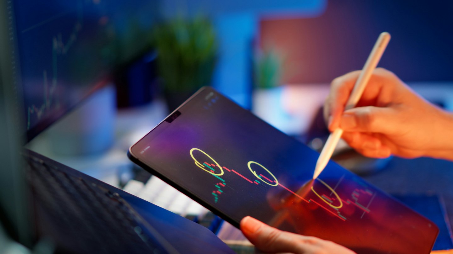 Hände analysieren mit einem digitalen Stift Finanzdiagramme auf einem Tablet.